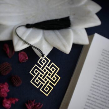 Metal bookmark featuring the Endless Knot, a Buddhist symbol of eternity and interconnectedness, on an open book.