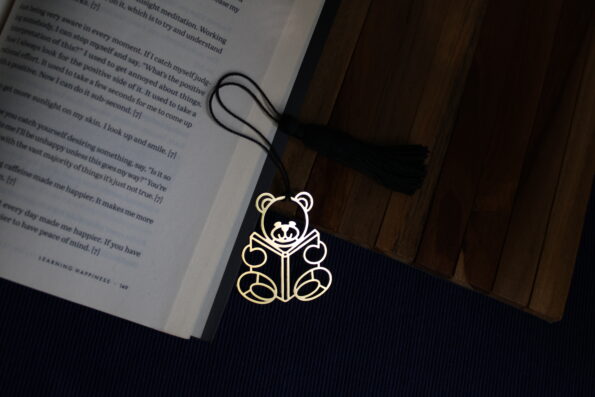 Charming brass teddy bear bookmark reading a book, with a black tassel.