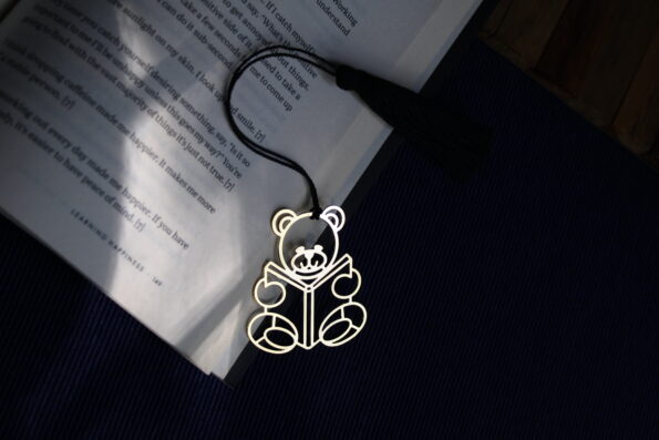 Charming brass teddy bear bookmark reading a book, with a black tassel.