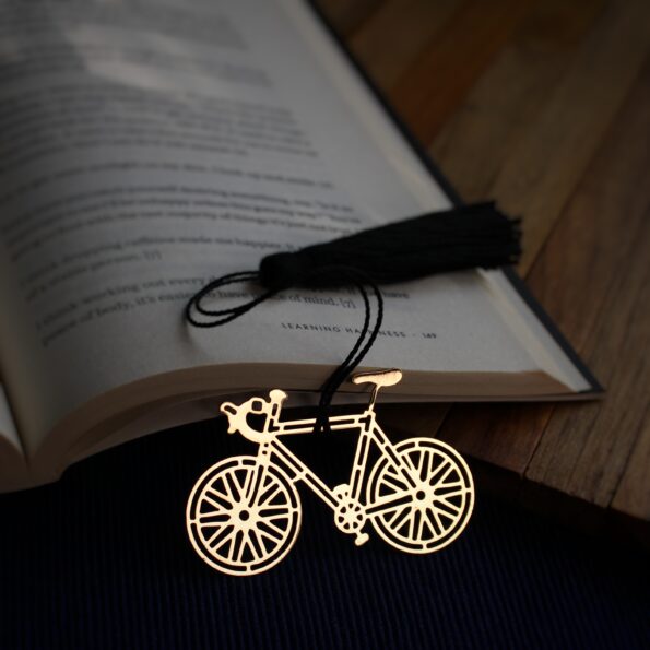Elegant brass bicycle design bookmark with intricate details and black tassel, resting on an open book.