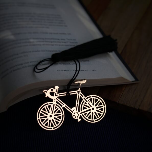 Elegant brass bicycle design bookmark with intricate details and black tassel, resting on an open book. 8