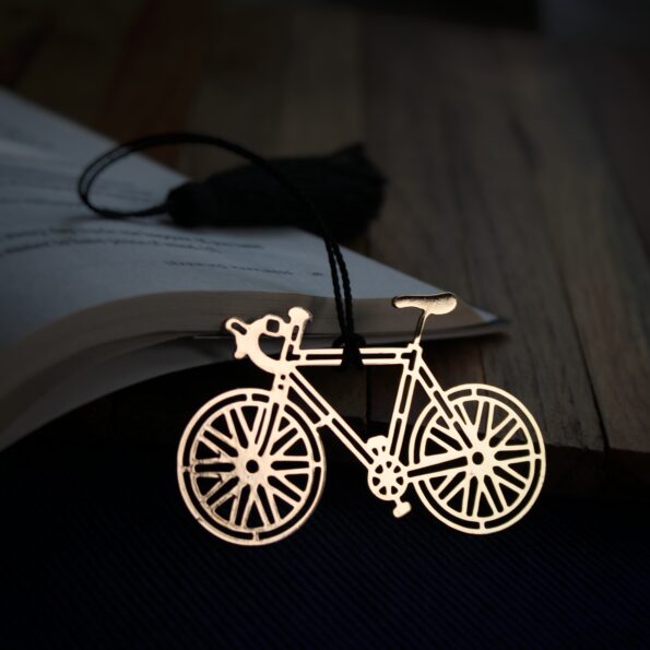 Elegant brass bicycle design bookmark with intricate details and black tassel, resting on an open book.