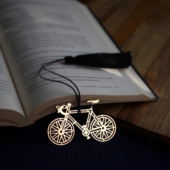 Elegant brass bicycle design bookmark with intricate details and black tassel, resting on an open book.