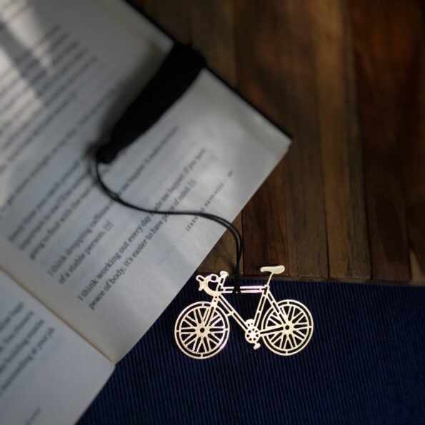 Elegant brass bicycle design bookmark with intricate details and black tassel, resting on an open book.