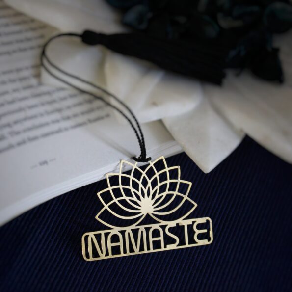 Brass Namaste bookmark with lotus flower design and black tassel on an open book.